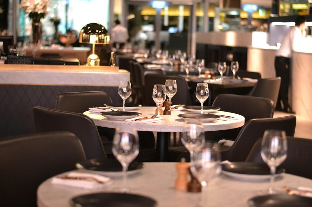 Elegant restaurant interior with round tables set for dining, featuring wine glasses, black plates, and soft lighting. Sophisticated and inviting ambiance.