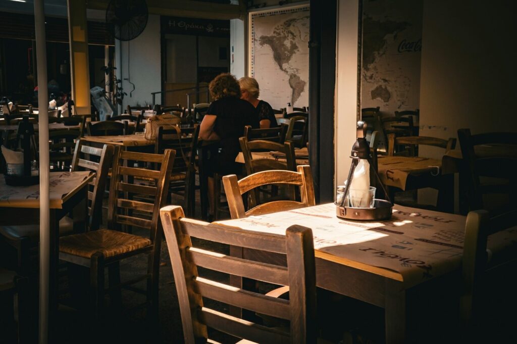 Cozy restaurant interior with wooden tables and chairs, low warm lighting. Diners sit in the background, and a world map decorates the wall.