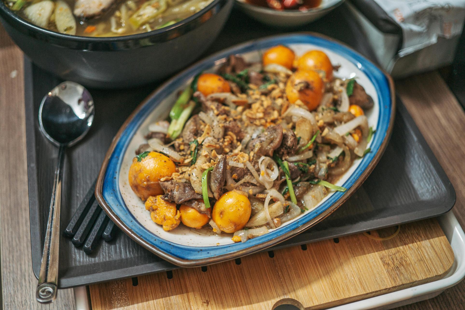 This image features a savory stir-fry dish served on an oval plate, consisting of meat, sliced white onions, green onions, and bright orange eggs, all topped with crispy fried garlic.
