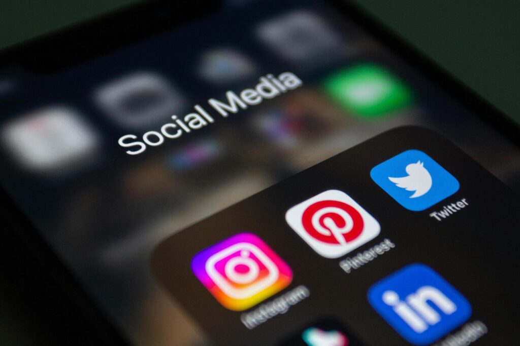 This image features a close-up of a smartphone screen displaying an open folder titled "Social Media" against a dark, blurred background. Inside the folder, popular application icons such as Instagram, Pinterest, Twitter, and LinkedIn are clearly visible and in sharp focus.