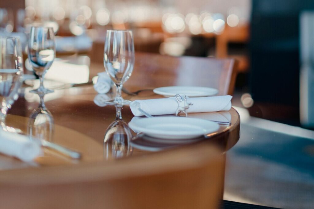 Elegant table setting with folded white napkins, shiny silverware, and sparkling glasses on a polished wooden table, creating a refined atmosphere.