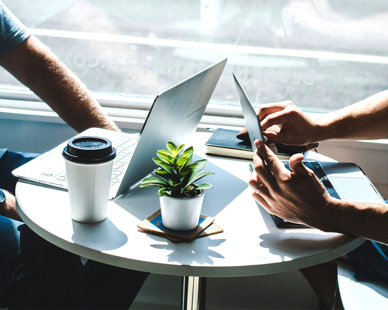 Two men seated at a table with a laptop, engaged in discussion and collaboration over a digital project.
