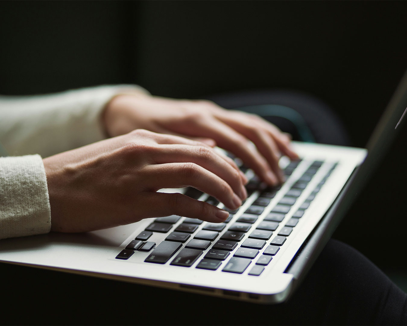 A pair of hands typing on a laptop keyboard at a desk, suggesting active work or content creation in progress.