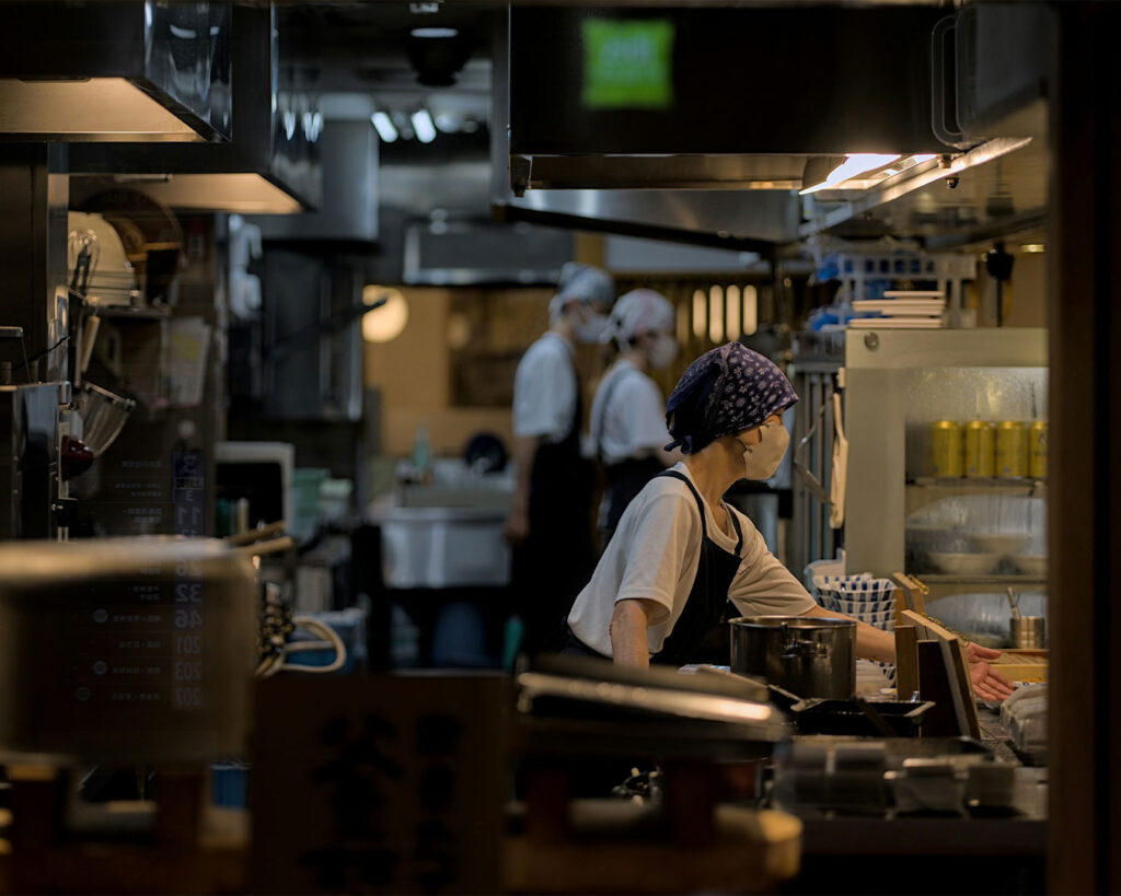 A kitchen staff member preparing food at the counter, surrounded by cooking tools and ingredients in a clean, busy kitchen environment.