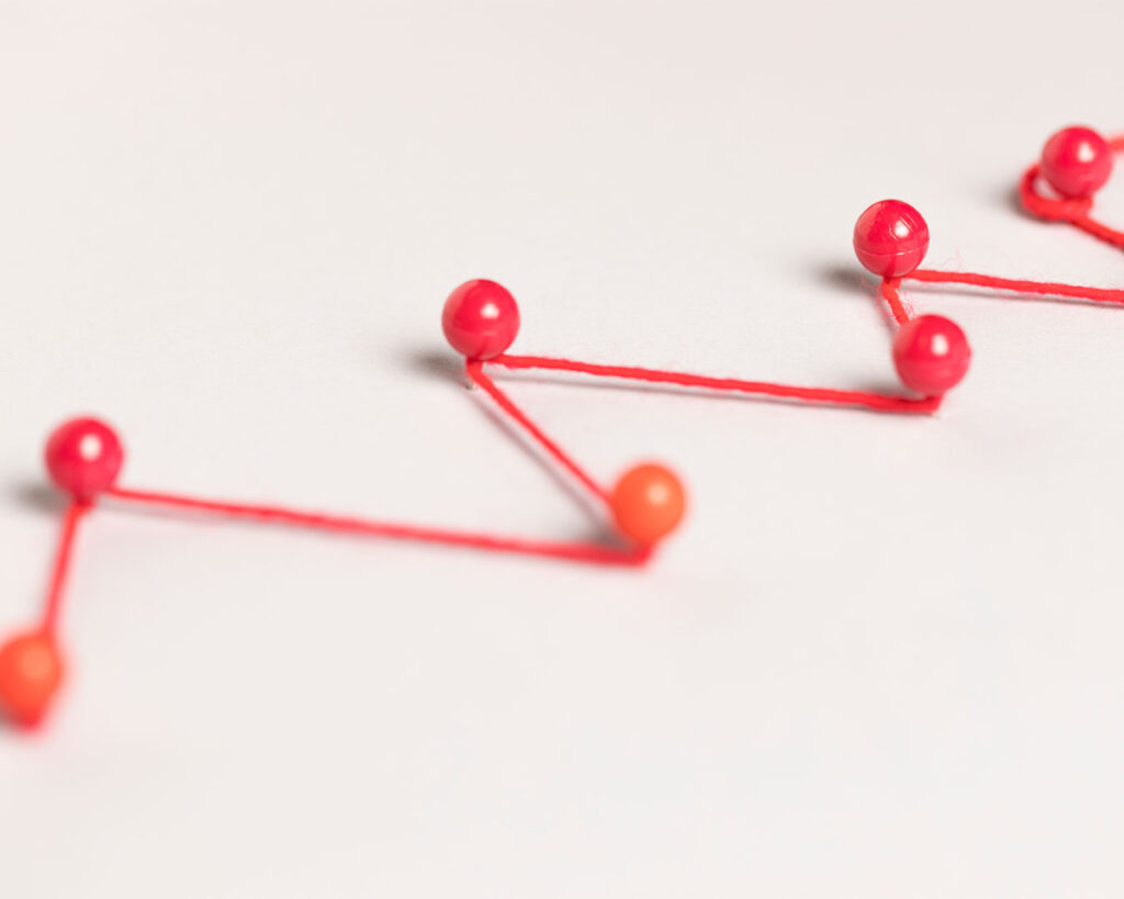 Coloured pins connected by threads on a board, illustrating a mapped-out roadmap that connects goals, milestones, and long-term planning paths.