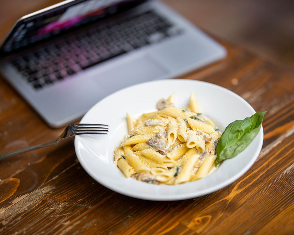 A plated dish set on a table next to a computer, showing a blend of dining and digital work in a modern, casual workspace setting.