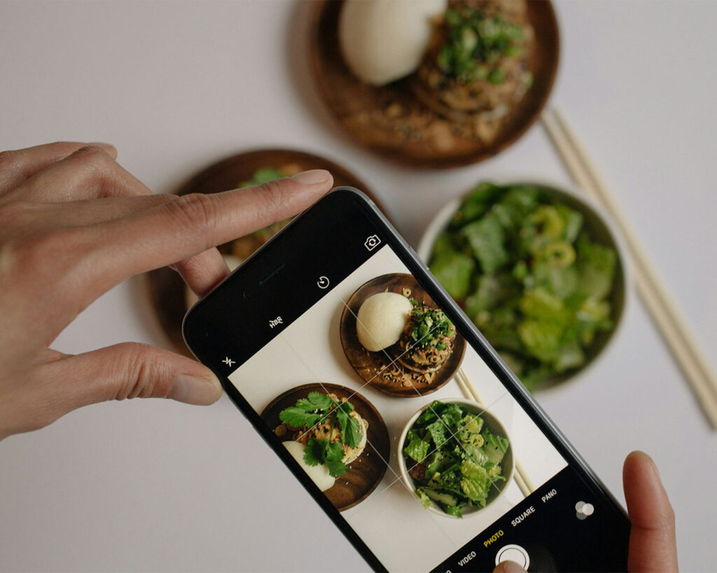 A hand using a smartphone to take a photo of a plated dish, highlighting food presentation and visual appeal.