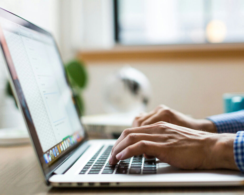 A close-up view of hands typing on a laptop keyboard, indicating focused work or digital activity in a workspace setting.
