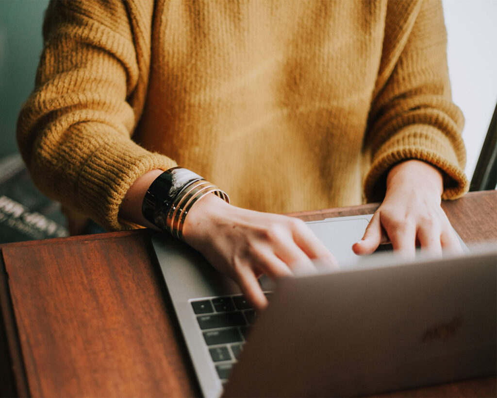 A woman sitting at a desk typing on her laptop, focused on her work in a calm and organised workspace.
