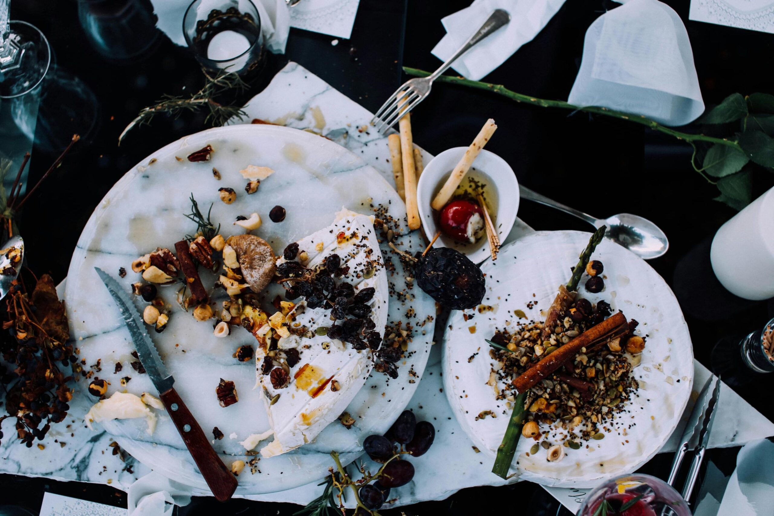 This overhead shot features an elegant, rustic spread of brie cheese, nuts, and dried fruits scattered across white marble platters.