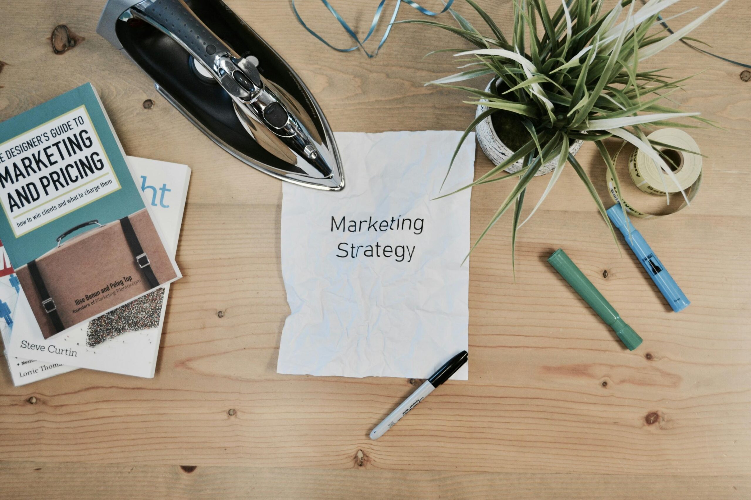 This top-down view shows a wooden desk arranged with business-related items, including books on marketing and a piece of crumpled paper labeled "Marketing Strategy."