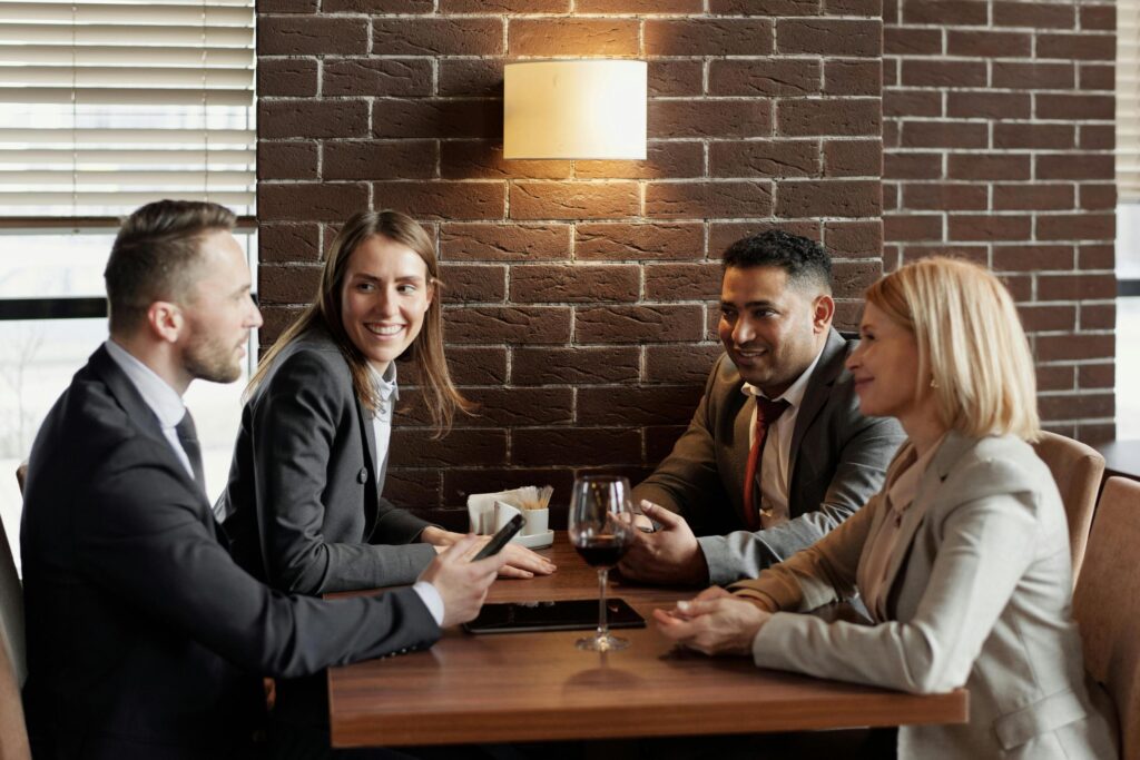 Four professionally dressed individuals are seated around a wooden table in a dimly lit restaurant, engaged in a lively conversation.