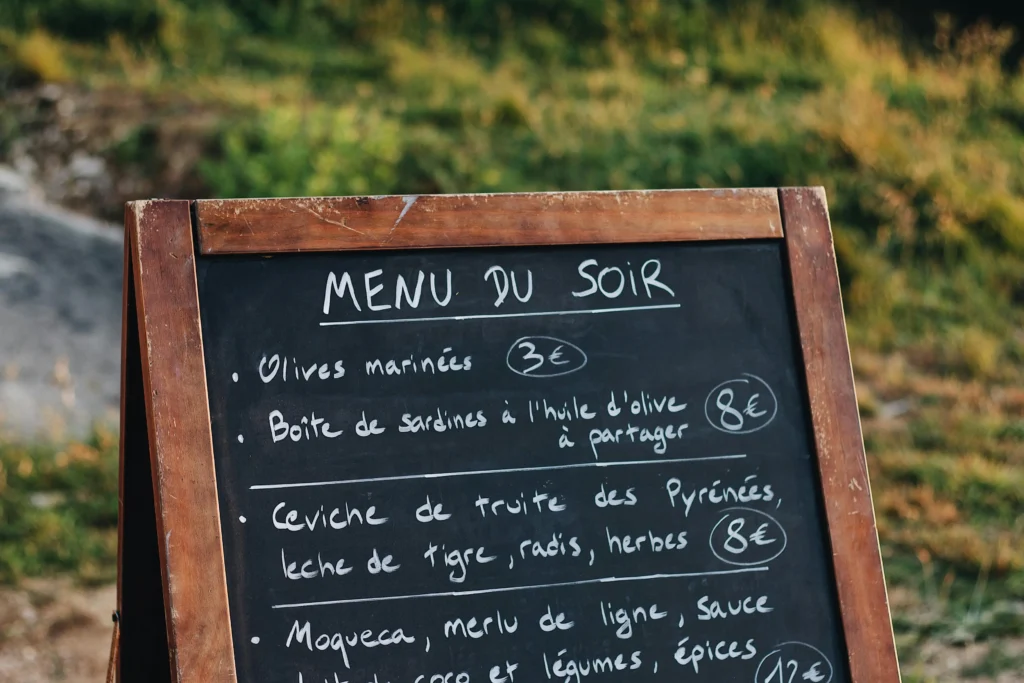 A hand-written chalkboard menu titled "MENU DU SOIR" displays various evening dishes and their prices in euros.
