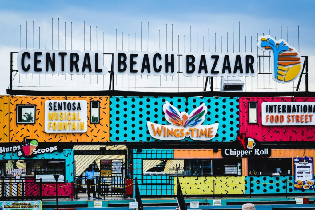 A vibrant, multi-colored bazaar facade features several shipping containers decorated with bold patterns and business signs. The main "Central Beach Bazaar" marquee sits atop the structure.