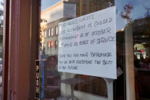 A handwritten note taped to a glass restaurant door announces its permanent closure as of October 2nd, after 22 years of service. The sign thanks customers for their patronage and wishes everyone the best in the future.
